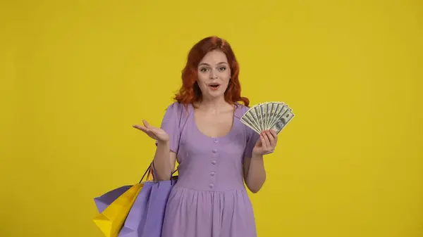 一个拿着购物袋的女人手里拿着一叠钞票 红头发的购物狂女人在工作室的黄色背景 广告领域 工作空间 — 图库照片