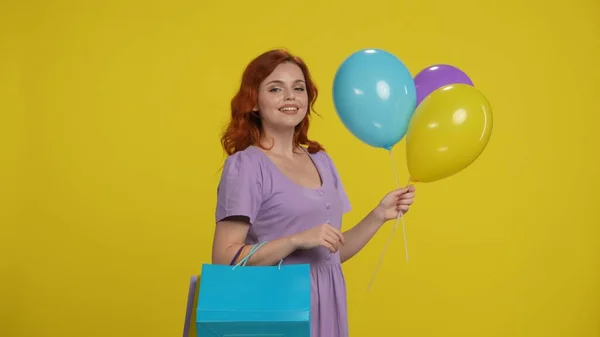ショッピングバッグとカラフルな風船を持つ陽気で幸せな赤毛の女性 黄色の背景にあるスタジオの女性 セール ブラックフライデー — ストック写真