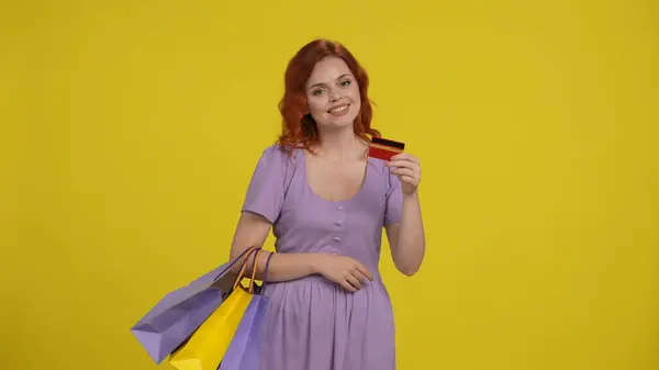 ショッピングバッグを持っている女性は笑顔でクレジットカードを持っています 黄色の背景にあるスタジオの日没の女性 — ストック写真