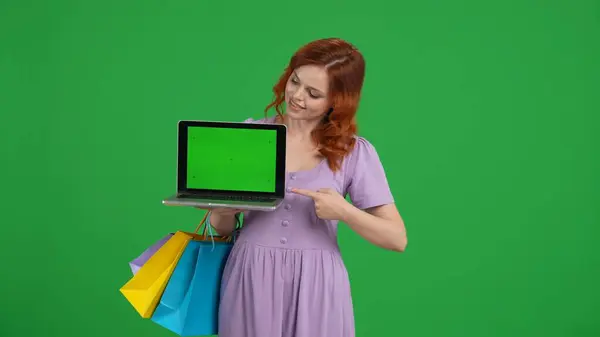 Молодая Женщина Пакетами Покупок Указывает Указательным Пальцем Зеленый Экран Ноутбука — стоковое фото