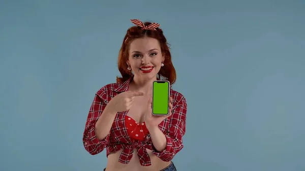 青い背景の青い女性のフレーム カメラを見て笑顔で 彼女の前に緑色のスクリーンが付いている携帯電話を保持し それを指摘します これはあなたの広告 あなたのプロダクトかもしれません — ストック写真