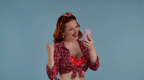 写真は青い背景に明るく色付けされたメイクをした若い赤毛の女性を示しています 彼女は携帯を見つめ 誰かにテキストを送っている さらなる描写は そして幸福である メディア — ストック写真