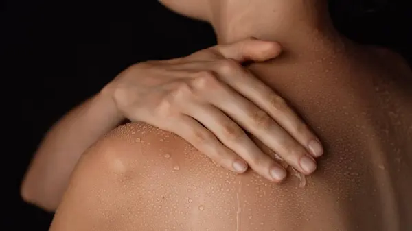 Skin texture and bodycare beauty concept. Portrait of female model. Closeup studio shot of beautiful woman body, touching skin with water drops on the shoulder back area after bathing.