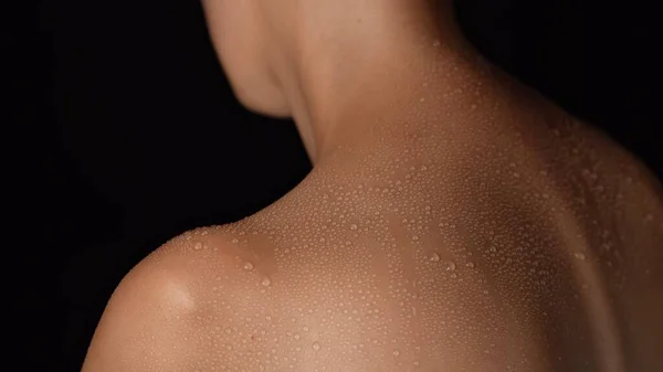 Skin texture and bodycare beauty concept. Portrait of attractive female model. Closeup studio shot of young woman body part, wet skin with water drops on the shoulder back area after shower.