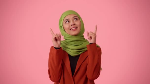 中規模の隔離されたビデオは ヒジャーブ ベールを身に着けている魅力的な若い女性をキャプチャします 彼女は上に何かを強調する指を指差している 広告のための場所 モックアップ プロモーション — ストック動画