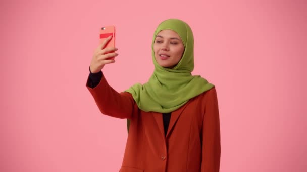 中規模の隔離されたビデオは ヒジャーブ ベールを身に着けている魅力的な若い女性をキャプチャします 彼女は自分自身の写真をスマートフォンで撮っている 多様性のための場所 — ストック動画