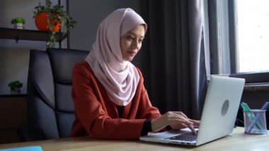 Orta boy video, tesettürlü, duvak takan çekici bir genç kadını çekiyor. Uzun bir çalışma ve vardiya gününden sonra laptopunu kapattı. Kültürel çeşitlilik, iş ve eğitim, reklam.