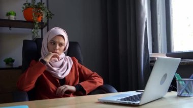 Orta boy video, tesettürlü, duvak takan çekici bir genç kadını çekiyor. Bilgisayarında çalışıyor ya da çalışıyor, bir şeyler düşünüyor. Kültürel çeşitlilik, iş ve eğitim, reklam.