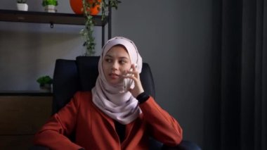 Orta ölçekli bir video, tesettürlü, duvak takan ve ofisteki sandalyede oturan çekici bir genç kadını çekiyor. Bir iş görüşmesi var. Kültürel çeşitlilik, iş ve eğitim, reklam.