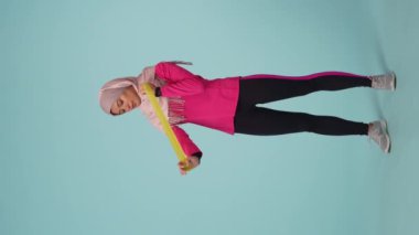 Tam ölçekli izole bir video, spor giyimli ve tesettürlü çekici bir genç kadın, Sheila. Lastik bant ile egzersiz yapıyor. Reklamınız için yer, modellik, promosyon, spor.