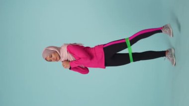 Tam ölçekli izole bir video, spor giyimli ve tesettürlü çekici bir genç kadın, Sheila. Lastik bant ile egzersiz yapıyor. Reklamınız için yer, modellik, promosyon, spor.