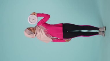 Tam ölçekli izole bir video, spor giyimli ve tesettürlü çekici bir genç kadın, Sheila. O bir saat tutuyor ve yüzüne dokunuyor. Reklam için yer, promosyon, spor.