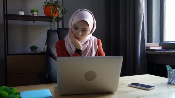 中等尺寸的视频拍摄了一个戴着头巾 头戴头巾的年轻貌美女子 她在笔记本电脑上工作或学习 思考着什么 文化多样性 就业和教育 — 图库视频影像