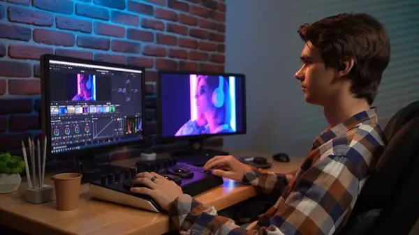Video and photo editing advertisement concept. Freelancer working from home. Portrait of young man in casual at the desk working on pc, looking in monitors, editing video with special equipment.