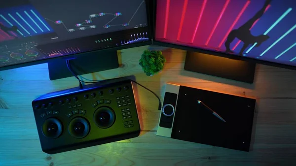 Video and photo editing advertisement concept. Freelancer workspace at home. Top view of the table with monitors with neon light, editing equipment for videos and photos, graphic tablet.