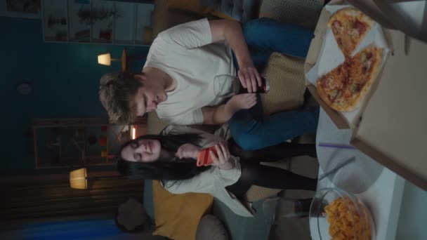 最初の愛と関係創造的なコンセプト 十代のカップルの肖像画は時間を費やしています ソファーに座ってスマートフォンを持ち ピザを食べ セルフィーの写真を撮る バーティカルビデオ — ストック動画