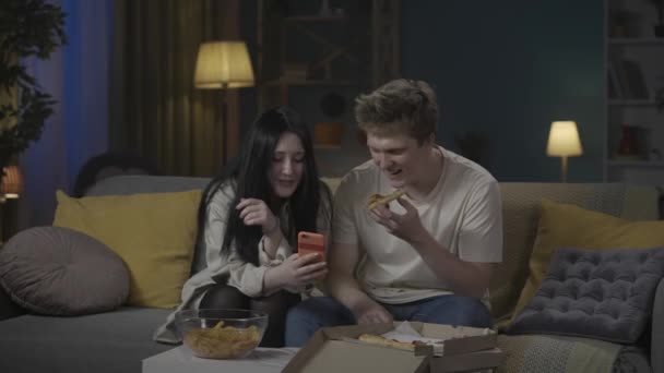 最初の愛と関係創造的なコンセプト 十代のカップルの肖像画は時間を費やしています ソファーに座っている男の子と女の子は ソーシャルメディアを見ているスマートフォンを保持し ピザを食べ セルフィー写真を撮る — ストック動画