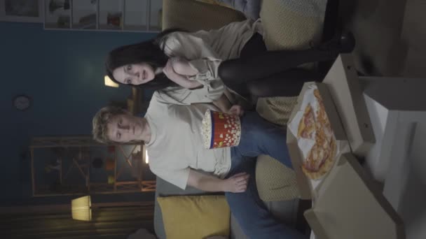 最初の愛と関係創造的なコンセプト ソファーに座ってポップコーンを食べ 映画を見ている少年と少女 少年は恥ずかしげに女の子の肩に手を置き 少女はハグを受け入れる バーティカルビデオ Hdr Bt2020について — ストック動画