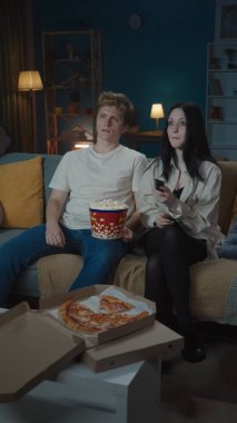 İlk ilişkiler yaratıcı konsept. Boş zamanlarını geçiren genç bir çiftin portresi. Kız ve erkek kanepede oturup patlamış mısır yiyor ve film izliyorlar. Dikey fotoğraf.