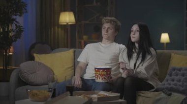 İlk aşk ve ilişkiler yaratıcı kavram. Genç bir çiftin portresi. Kız ve erkek kanepede oturup patlamış mısır yiyor ve film izliyorlar. Oğlan kıza sarılmaya çalışır ama kız reddeder. HDR BT2020