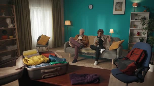 一个年轻人的视频 他和他的祖父 爷爷坐在沙发上 沙发上 用他们的智能手机 分享一些东西 打开前置的行李箱 搬到一个新的地方 — 图库视频影像