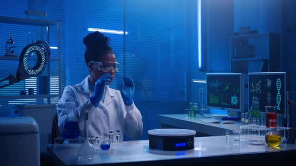 中等尺寸的视频记录了一位戴着眼镜和实验室外套的女科学家坐在实验室里 研究你在他们面前展示的全息图 扩大的现实 — 图库视频影像
