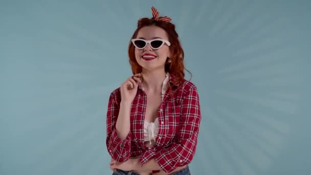 Kadrze Młoda Kobieta Niebieskim Tle Patrzy Kamerę Okularach Przeciwsłonecznych Kręci — Wideo stockowe