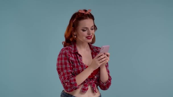 在蓝色背景的镜框里 年轻的红头发女人有着明亮的妆容 她看着自己的手机 通过视频链接热情地与人交谈 她很喜欢对话 微笑着 — 图库视频影像