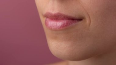 Deri dokusu ve güzellik konsepti. Güzel bir modelin portresi. Makro beyaz kadın pozu. Yüzünün bir kısmı makyajsız. Dişi pembe dudakların yakın çekimi, görünür dişleri ve diş etleriyle gülümsüyor..