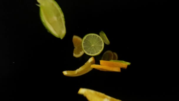 下のビューは 緑色のライムとオレンジ色のスライスが上からカメラに落ちる多くをキャプチャする孤立したマクロ撮影です ブラックバック レストラン広告 — ストック動画