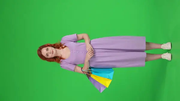 一个红头发的女人提着购物袋 用食指向上点 点头表示同意 全长女性在工作室的绿色屏幕上 垂直录像 广告区 工作区 — 图库照片