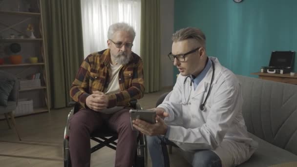 집에서 환자의 상태를 의사의 비디오 태블릿에 뭔가를 보여주는 휠체어에 노인과 — 비디오