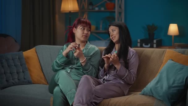 影片中 两个身穿睡衣的年轻女子坐在房间的沙发上 闲聊着 一边整理指甲 一边画指甲 一边谈论着什么 女孩之夜 过夜者 — 图库视频影像
