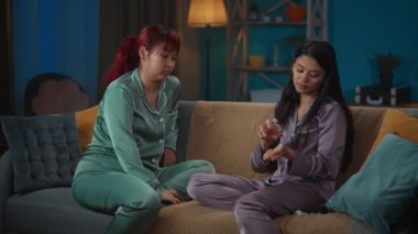 Pijamayla kanepede oturan iki genç kadının, birinin bileğindeki parfümü koklarken orta boy videosu. Kızlar aromayla ilgili aynı fikirleri paylaşmazlar..