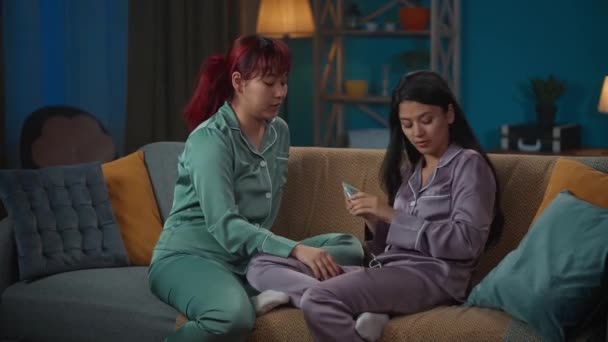 画面中 两个穿着睡衣的年轻女子坐在沙发上闲聊着 一边谈论着某件事 一边在用护手霜 女孩之夜 过夜者 — 图库视频影像