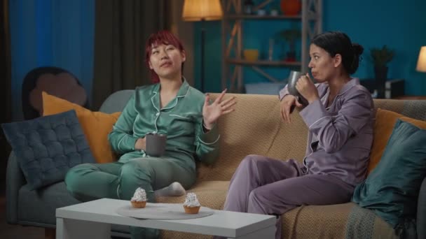 视频中 两个穿着睡衣的年轻女子坐在房间的沙发上 喝着杯子里的咖啡 聊着什么 女孩之夜 过夜者 兄弟姐妹 — 图库视频影像
