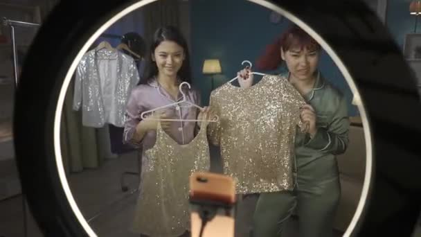 从环光灯内拍摄的全长视频拍摄到两名年轻女性用智能手机拍摄自己 她们在衣架上展示出不同的衣服 并进行现场直播 时尚博客 — 图库视频影像