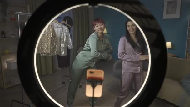 全尺寸的视频镜头从环光灯内拍摄到两名年轻女子跳舞时在房间里拍摄自己的照片 背景上挂着稀奇古怪的服装 社交网络 — 图库视频影像