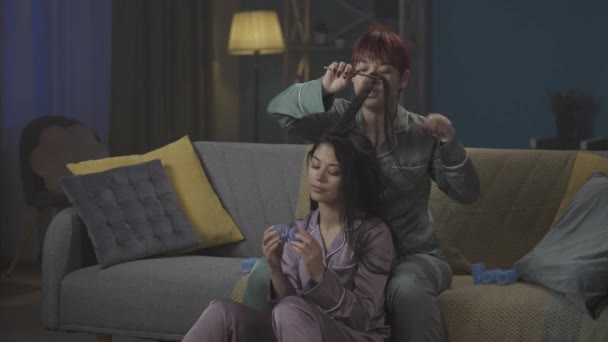 中完整的视频记录了两个穿着睡衣坐在沙发上的年轻女性 她们一边谈论某件事 一边在做另一个人的头发 女孩之夜 过夜者 兄弟姐妹 — 图库视频影像
