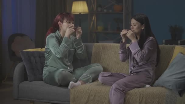 ソファーに座って夜のスキンケアのルーチンをしたり リップパッチを着てパジャマを着た2人の若い女性を撮影する中フルビデオ ガールズナイト 睡眠オーバー — ストック動画