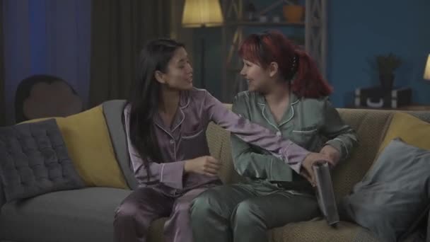 中完整的视频记录了两个穿着睡衣坐在沙发上的年轻女性 翻阅相册 回忆她们的童年 女孩之夜 过夜者 兄弟姐妹 — 图库视频影像