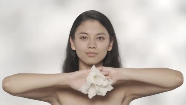 美容美发广告的概念 服装工作室拍摄美丽的女模特 布伦内特姑娘手里拿着白花 面带微笑地捧着花朵在耳边摆姿势 触摸着她的脸 Hdr — 图库视频影像