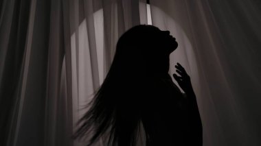 Havluya sarılmış, vücudunu, boynunu okşayan ve boğuk bir ışıkta saçlarını okşayan genç bir kadının orta boy fotoğrafı. Ürün reklamı, kişisel bakım rutini.