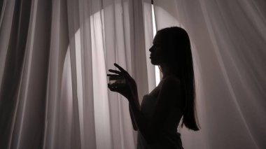 Havluya sarılmış genç bir kadının vücut, yüz kremi kavanozu, boğuk bir ışıkta güzellik malzemesi tutarken orta ölçekli bir yan görüntüsü. Ürün reklamı, kişisel bakım rutini.