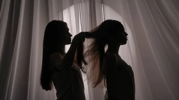 两个姐妹 用毛巾包裹的年轻女人的侧影 其中一个是在柔和的光线下编织另一个人的头发 产品广告 自我护理常规 — 图库照片