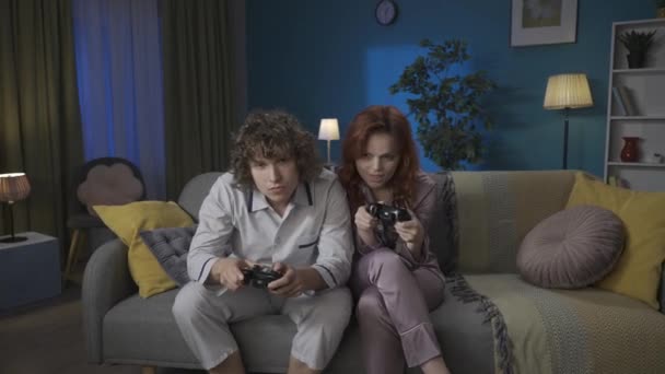 家族と人間関係の広告コンセプト 一緒に過ごした若いカップルの肖像画 ソファーに座り ビデオゲームをしたり 冗談で戦ったりするパジャマの男女が勝った Hdrについて — ストック動画