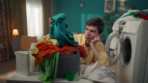 洗濯機の隣に座っている暗い髪の男は 洗濯バスケットを見て 彼女がしなければならない家事について疲れました 広告など — ストック動画