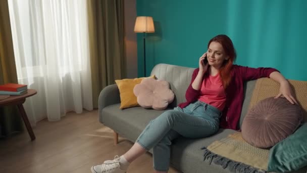 Uzaklaş Kanepede Oturan Kızıl Saçlı Kadın Telefonda Çamaşır Makinesiyle Ilgili — Stok video