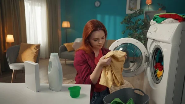红头发的女人从洗衣机里卸下洗好的衣服 检查衣服上是否留有污迹 家用电器 家务活 促销和广告 — 图库照片