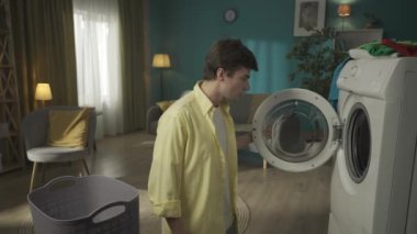 Koyu saçlı bir adam çamaşır makinesinin yanında duruyor, onu boşaltıyor. Elbiseler sırılsıklam olmuş, adam makinenin kurutmayı tamamlayamadığını düşünüyor. Ev aletleri, ev işleri, reklam.